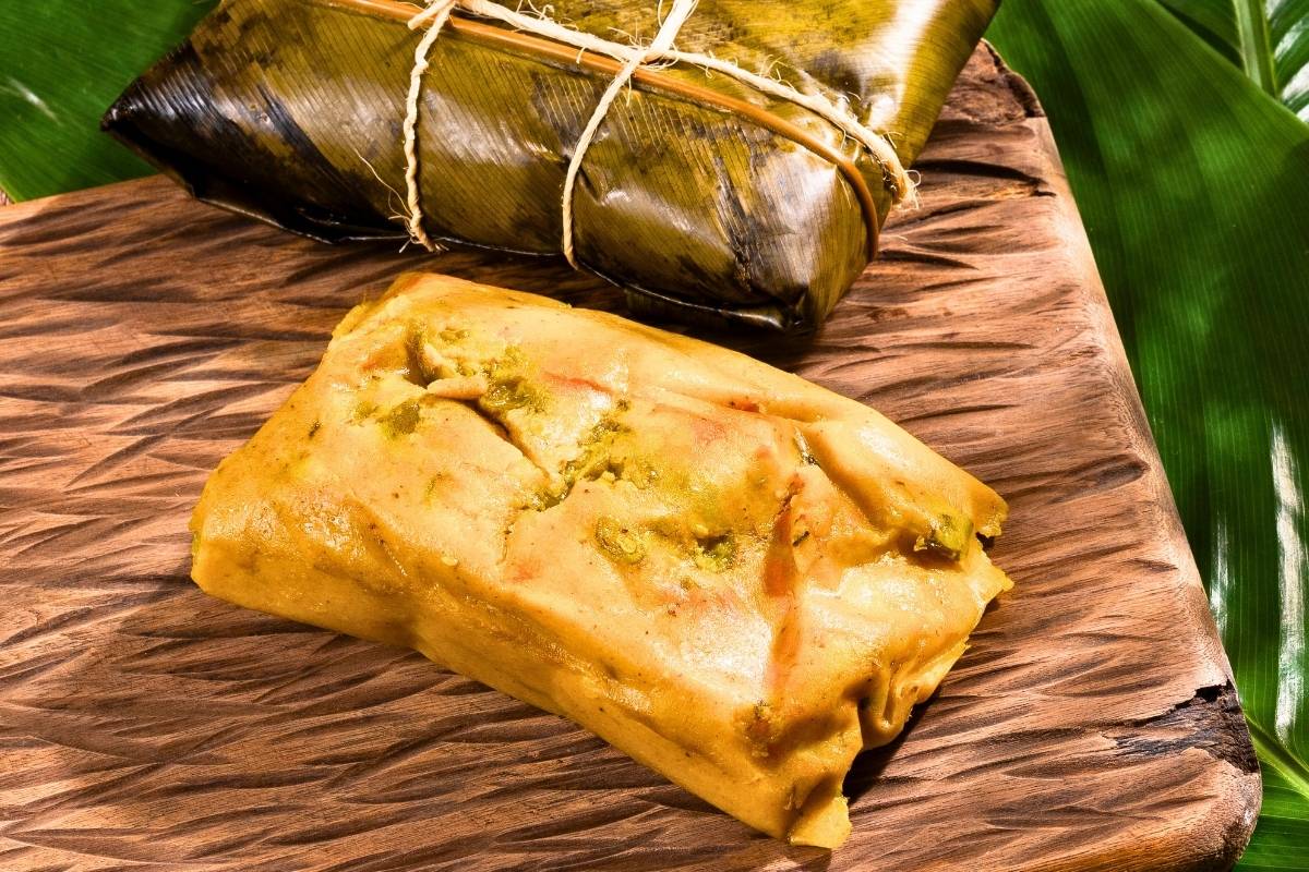 One open Tamale on a table and another  tamale in banana leaves.