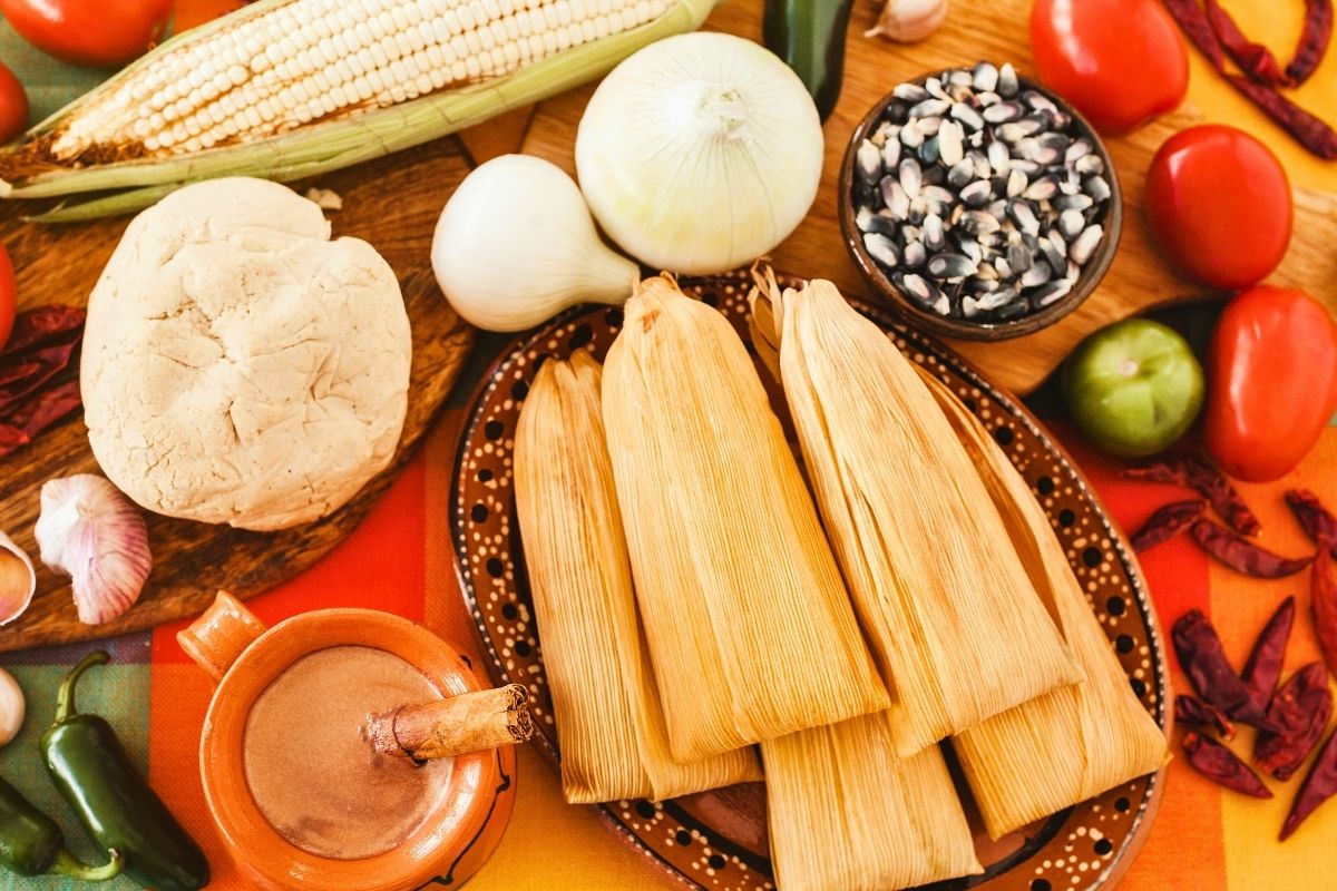 Five Tamales in a plate with other ingredients in bowls on the side.