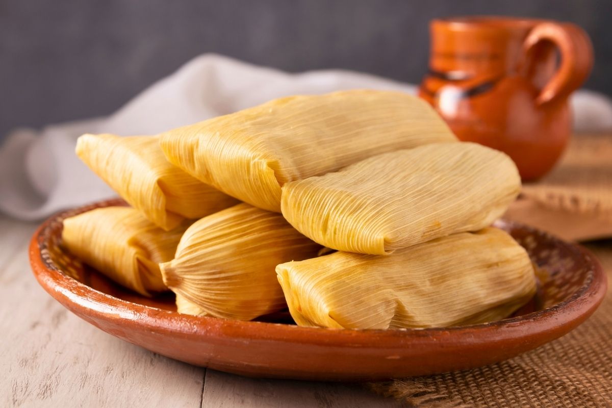 A brown clay dish of Tamales wrapped in corn leaves.
