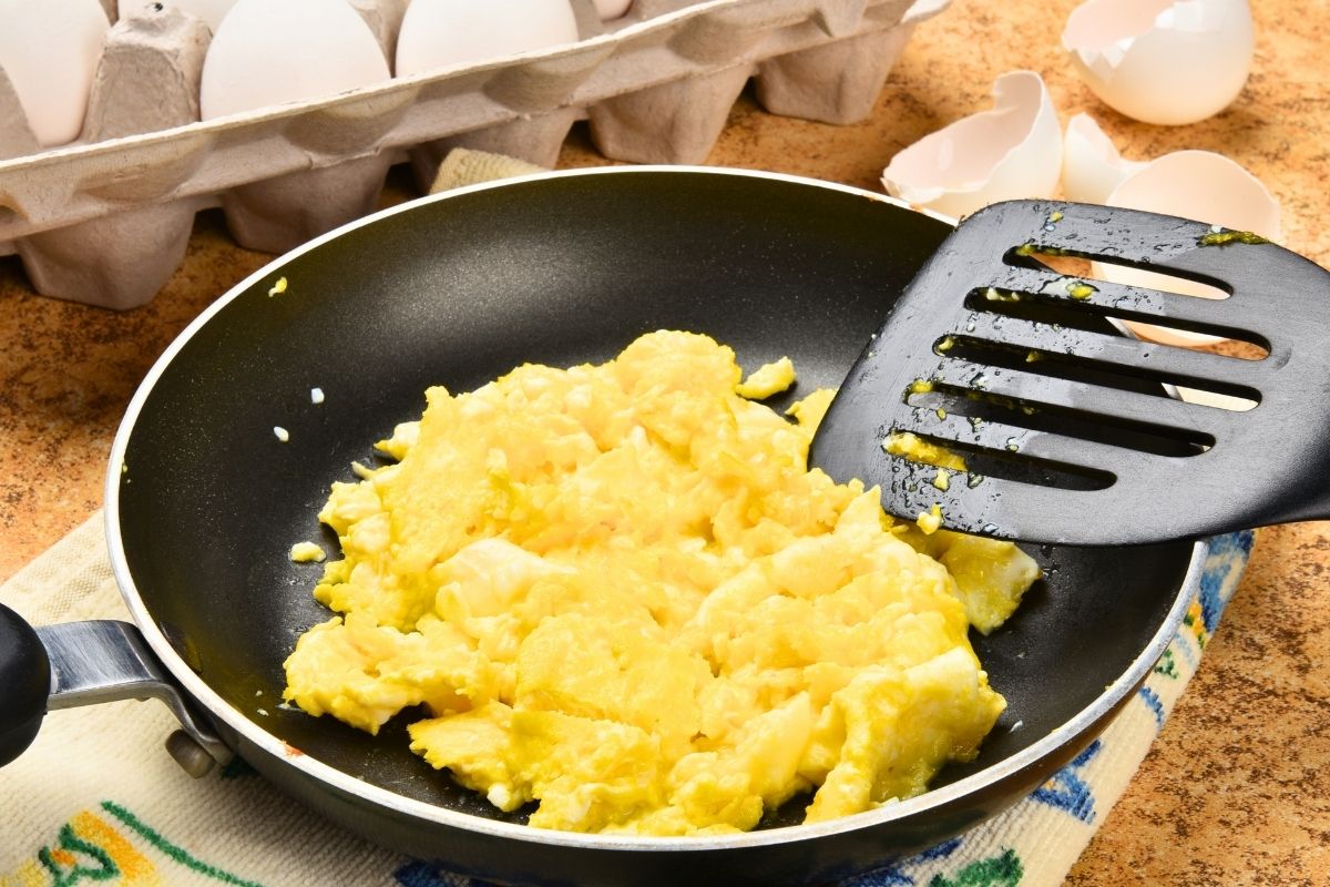 Scrambled eggs in a frying pan near the egg carton.