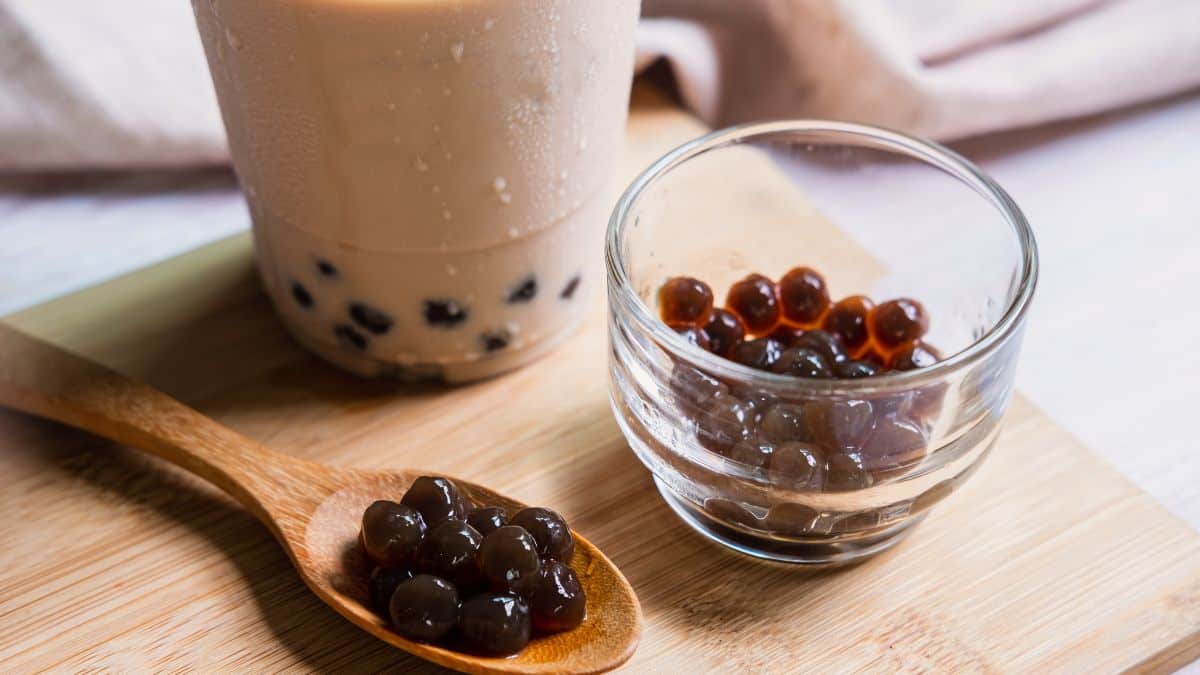 A spoon and bowl of black tapioca pearls with glass of bubble tea.