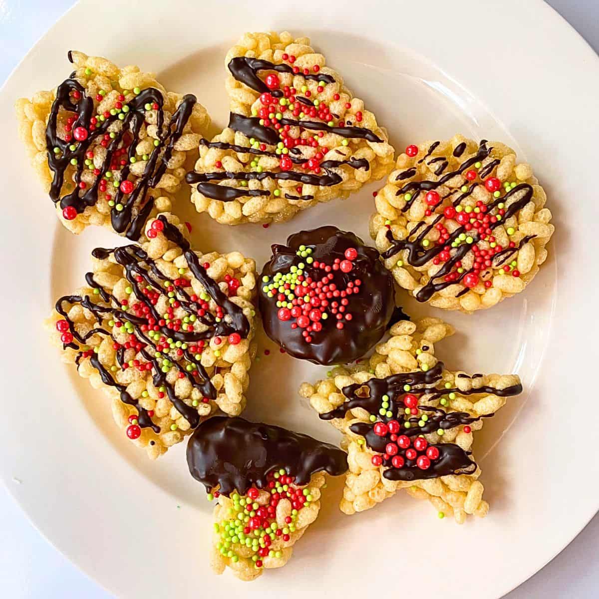 Holiday rice crispy treats with chocolate and sprinkles on a white plate.