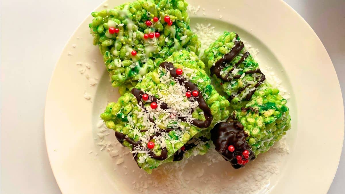Green rice krispies treats with chocolate and red candy balls on a white plate.