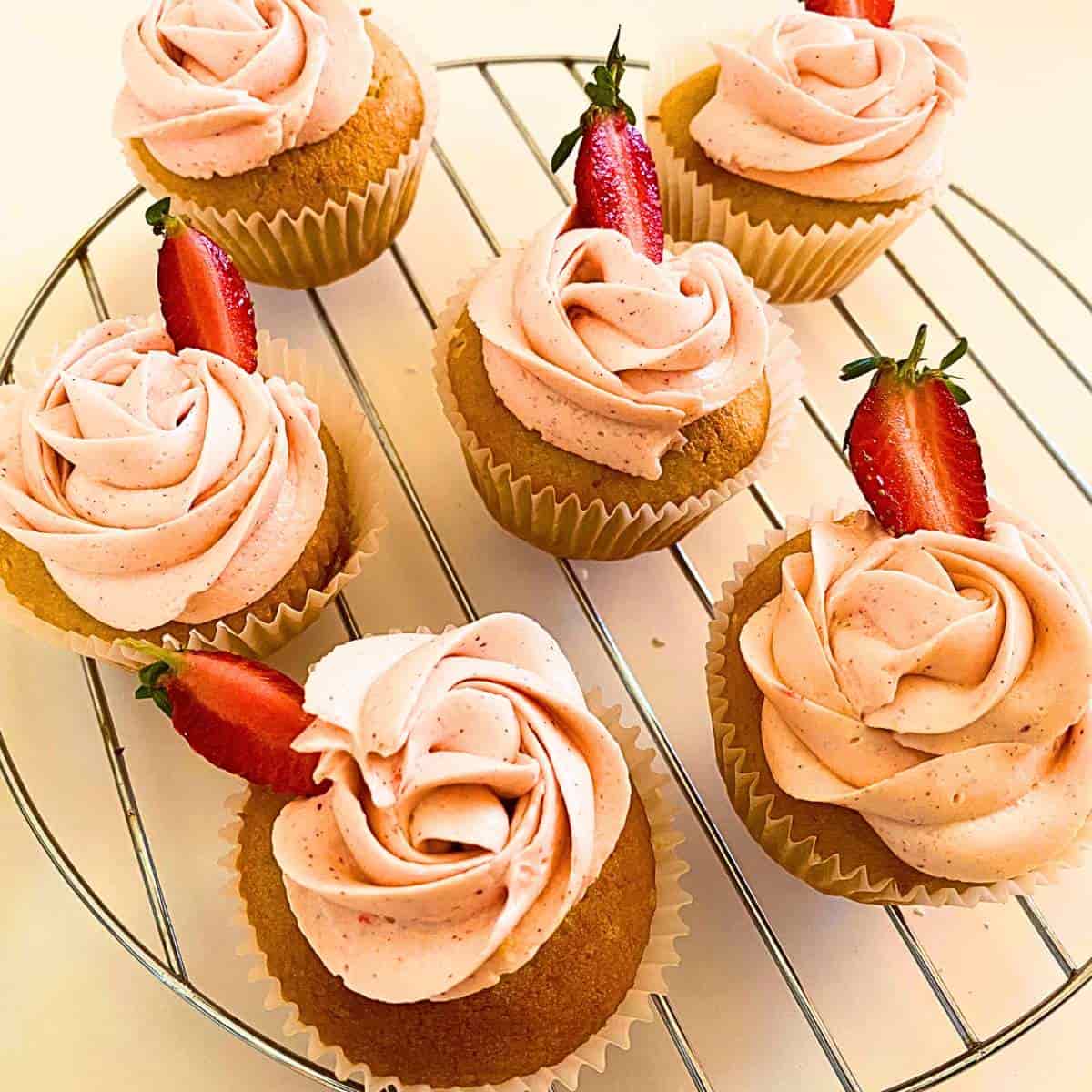 a group of cupcakes with pink frosting and strawberries on a metal rack