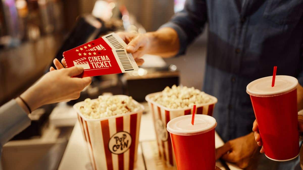 A person handing a ticket to a couple red buckets of popcorn.
