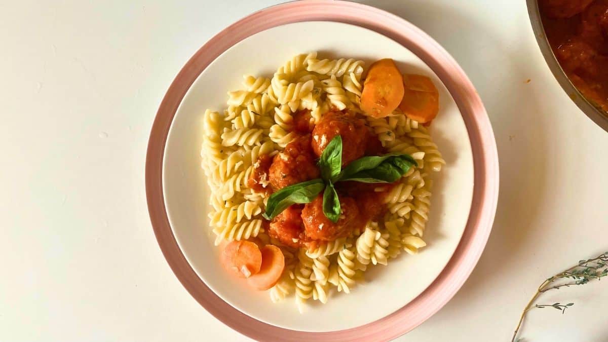 Pasta and meatballs on a white plate with garnish on it.