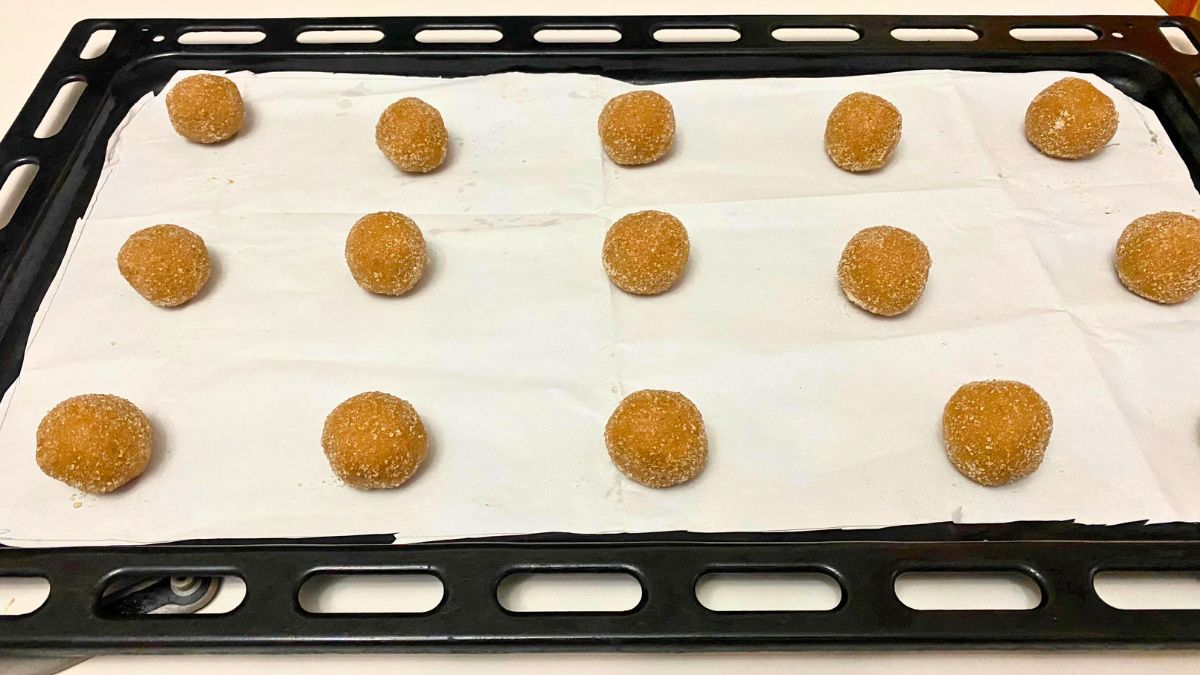 A baking tray with cookie dough on a white baking paper.