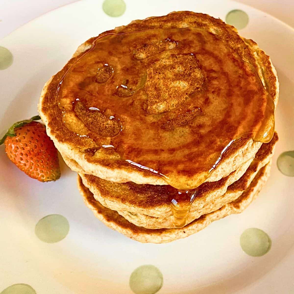 A close up of a stack of pancakes with a strawberry on the side.