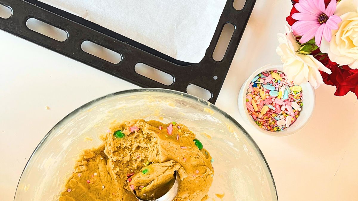 A bowl of cookie mix, a bowl of sprinkles and a baking tray.